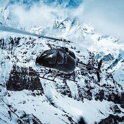 Schwarzer Hubschrauber vor schneebedeckten Bergen